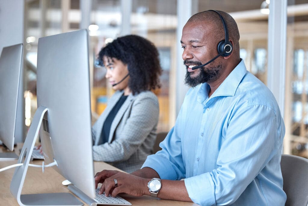 Two customer support specialists wearing headsets working at computers in an office