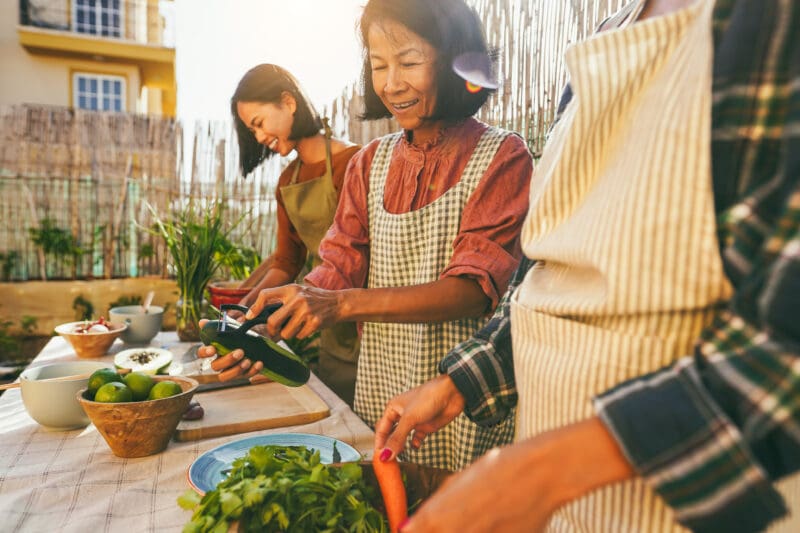 Three women preparing vegetables together outdoors at a table