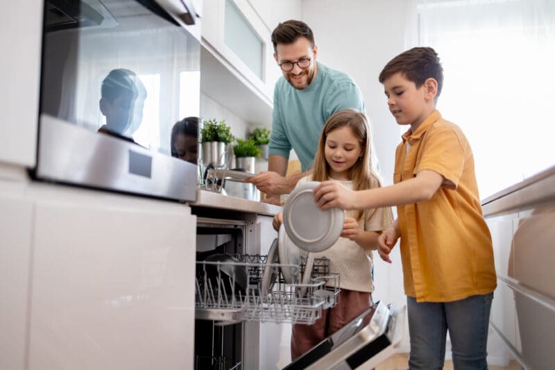 Father and two children loading dishes into a dishwasher in a modern kitchen