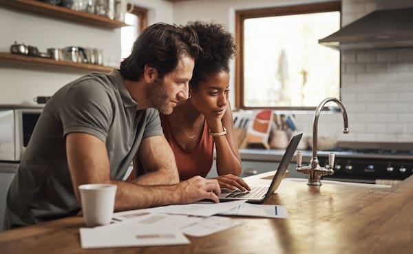 Couple reviews household bills together on a laptop at their kitchen counter
