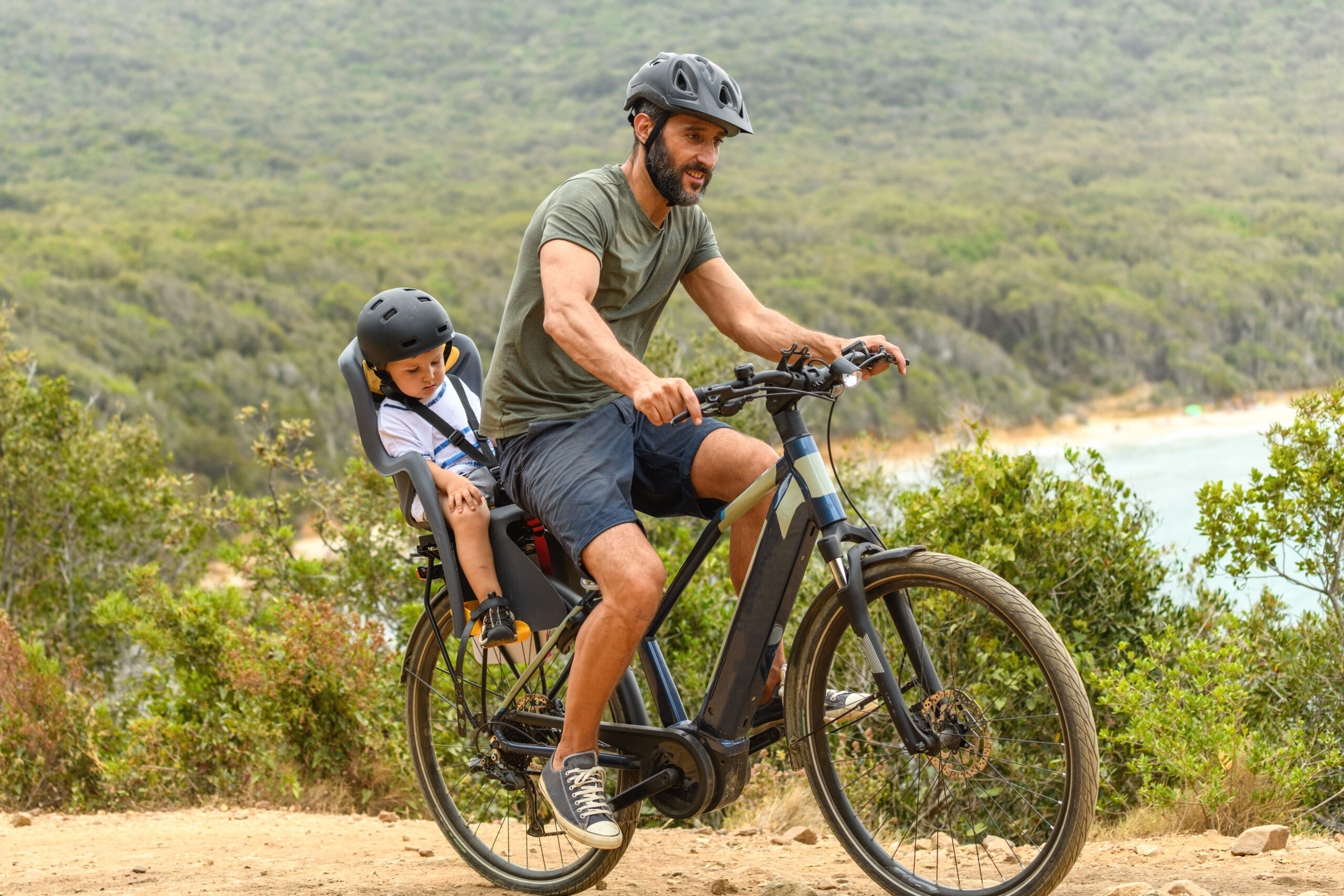 Adult riding an electric bike on a trail with a young child seated in a rear-mounted child seat